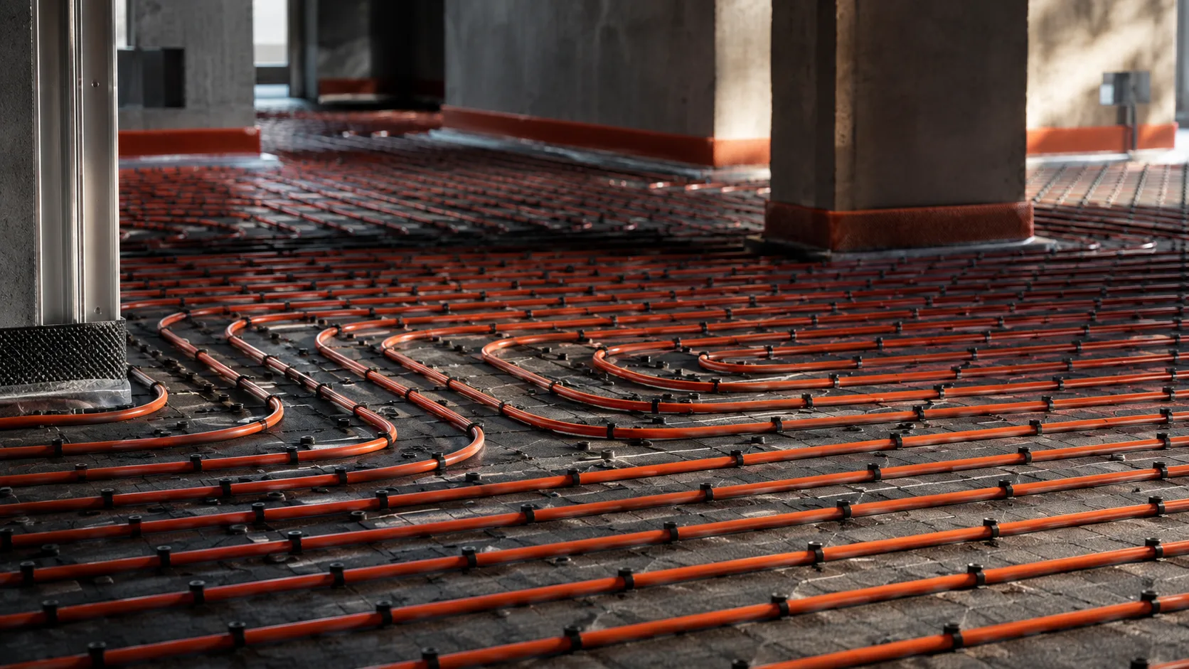 Fußbodenheizung — orange Heizrohre und Betonpfeiler in sonnendurchfluteter Halle